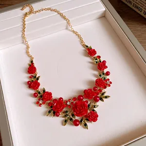 Close-up detail of a vintage floral necklace featuring red roses and green leaves