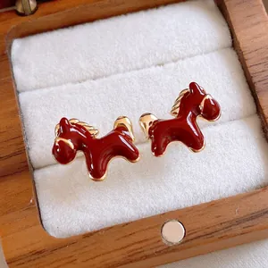 Detailed view of red enamel horse stud earrings in a wooden jewelry box.