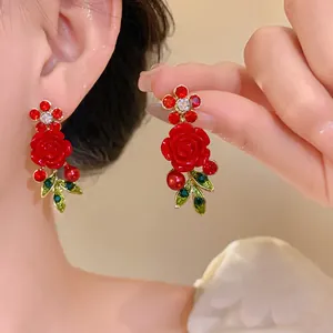 Detailed view of red rose earrings with rhinestones and green leaves