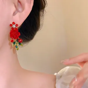 Close-up of elegant red rose and green leaf earrings with sparkling rhinestones