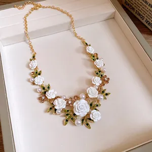 Close-up of elegant floral necklace with white roses, green leaves and pearls.