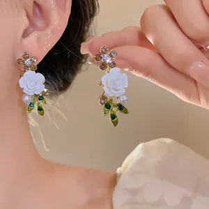 Detailed macro view of floral earrings featuring white roses and green enamel leaves