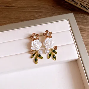 Macro detail of elegant floral earrings with white roses, green leaves, and pearls