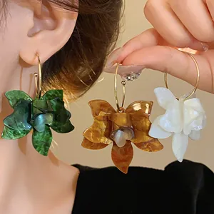 Detailed view of three resin flower hoop earrings in green, amber, and white colors