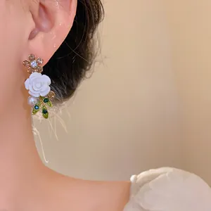 Detailed view of elegant floral earrings with white rose, rhinestones, and pearls on model.