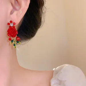 Close-up of elegant red rose and leaf earrings with rhinestones and pearl on ear