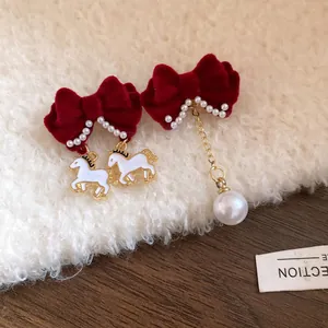 Asymmetrical red velvet bow earrings featuring white horse pendants and a gold chain pearl