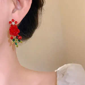 Close-up of elegant red rose and green leaf earrings with fine rhinestone details.