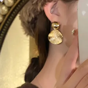 Primo piano di eleganti orecchini a pendente in metallo dorato martellato indossati da un modello