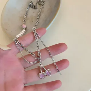 Detailansicht der silbernen Herz-Halskette mit weißen Perlen und rosa kirschförmigem Anhänger.