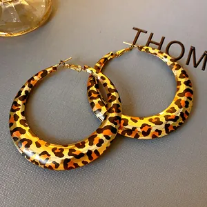 Macro view of geometric U-shaped leopard print hoop earrings on textured grey background