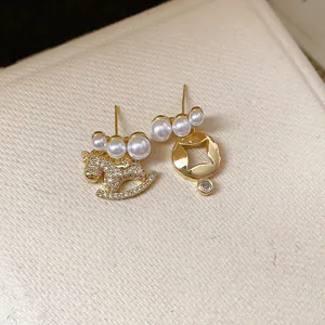Elegant asymmetric gold earrings featuring a zircon rocking horse and pearls on beige texture