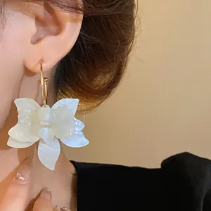 Close-up of elegant white resin flower earring with golden hoop on model