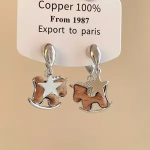 Macro view showing the intricate rocking horse and star charms of these silver-toned earrings