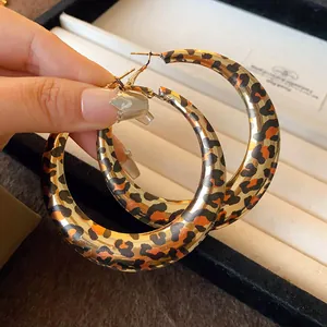 Close-up of exaggerated leopard print U-shape hoop earrings held by hand for scale