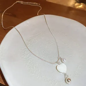 Nahaufnahme einer silberfarbenen Halskette mit herzförmigem Muschel-Anhänger und Perlendetails