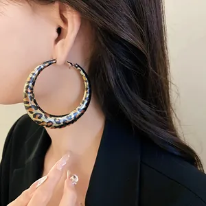 Close-up detail of a large leopard print geometric hoop earring worn by a model