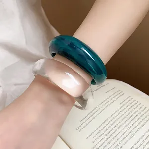 Dettaglio di bracciali rigidi in resina marmorizzata e acrilico trasparente al polso