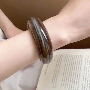Dettaglio di un bracciale rigido in acrilico marmorizzato marrone indossato al polso