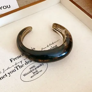 Primo piano di un bracciale rigido in resina marmorizzata con finitura tartarugata liscia.