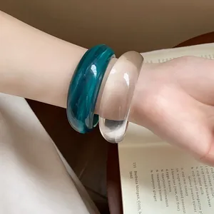 Primo piano di un paio di grossi bracciali in resina verde petrolio e trasparente