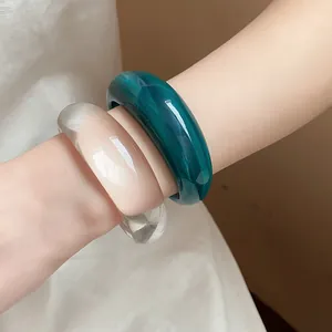 Dettaglio di grossi bracciali in resina verde marmorizzata e bianco traslucido al polso.
