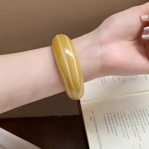 Bracciale rigido largo in resina con motivo marmorizzato giallo sul polso di un modello