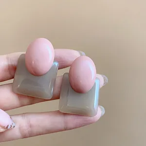 Detailed macro shot of vintage pink and gray oval square resin earrings on hand