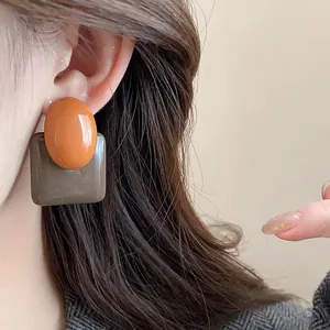Close-up of vintage resin stud earrings with orange oval and brown square shapes.