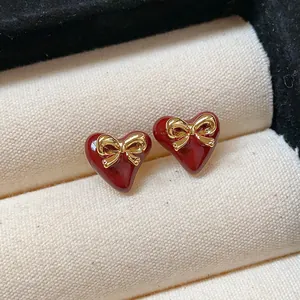 Close-up of elegant red heart stud earrings featuring golden bow accents on cream jewelry box