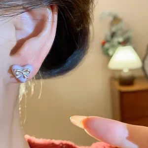 Close-up of a sweet purple heart stud earring with a silver bow detail worn on an ear