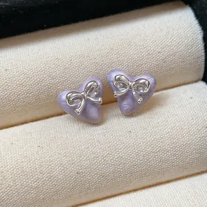 Elegant macro view of purple heart-shaped stud earrings featuring silver bowknot accents