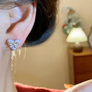 Macro view of purple heart-shaped stud earring with a silver bow worn on an ear