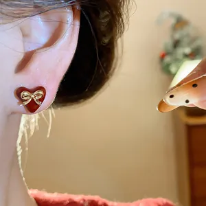 Detailed view of red heart stud earrings with golden bow detail worn on ear lobe.