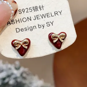 Close-up detail of elegant red heart stud earrings with a delicate gold bow design