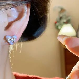 Close-up detail of sweet purple heart-shaped stud earring with a silver bow on ear