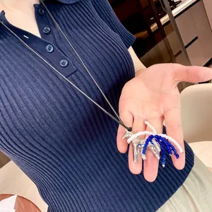 Detail showing a silver horse pendant with blue and white beaded tassels on a hand.