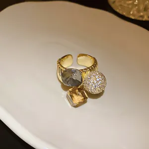 Detail of gold-plated open ring featuring gray crystal, amber stone, and zircon pave ball.