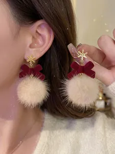 Detalle de pendientes navideños con copo de nieve, lazo de terciopelo rojo y pompones.