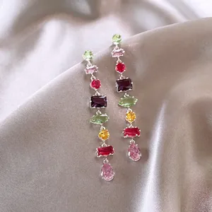 Close-up detail of colorful zircon tassel drop earrings on luxurious silk fabric background.