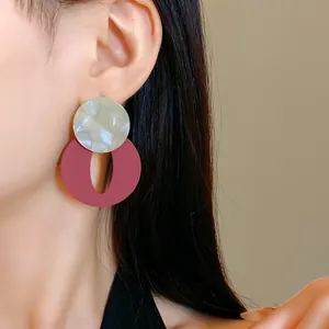 Close-up of retro acrylic earrings with marbled circle and maroon oval on a model