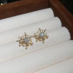 Primer plano de pendientes de copo de nieve dorados con brillantes y perlas blancas.
