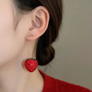Elegant red rhinestone strawberry dangle earrings worn by a model in a red sweater