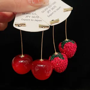 Close-up of sparkling rhinestone strawberry and glossy cherry earrings on cards
