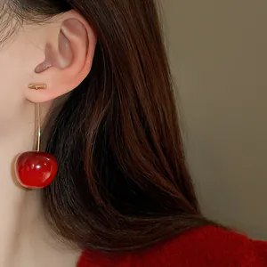 Detailed close-up view of a realistic red cherry drop earring with gold stud on a model's ear