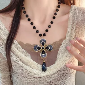 Vintage floral cross pendant necklace with black beads and gold finish worn by model