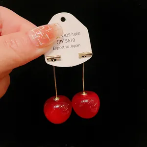 Detailed view of sweet red cherry drop earrings with gold-tone metal stems on white card