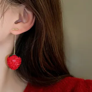 Close-up detail of a sparkling red rhinestone strawberry earring worn on the ear