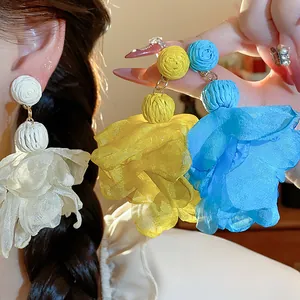 Dettaglio di orecchini a fiore colorati in rafia e chiffon in bianco, giallo e blu.