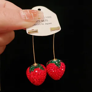 Macro view of sparkly rhinestone-encrusted strawberry dangle earrings on display card